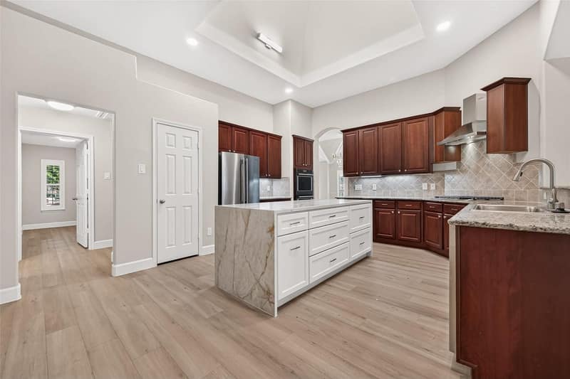 Kitchen with a marble waterfall island, double ovens and a vent hood